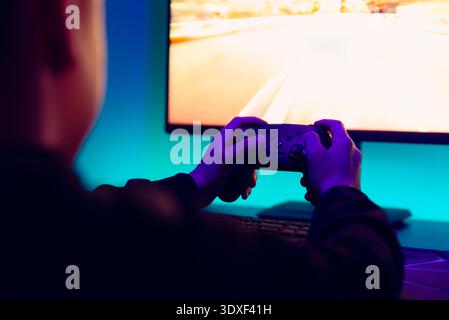 Over the shoulder view of gamer playing high speed racing video game on desktop monitor with colorful RGB lighting Stock Photo