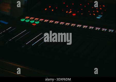 Riga, Latvia - February 28, 2026:Close-up of a professional audio mixing console with illuminated buttons and faders in a dark studio. Ideal for conce Stock Photo