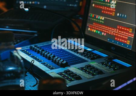 Riga, Latvia - February 28, 2026:Close-up of a professional lighting control console with illuminated faders and digital interface screens in a dark s Stock Photo