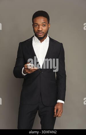 Young Man Stands in Suit Holding Smartphone Against a Neutral Background in a Studio Setting Stock Photo