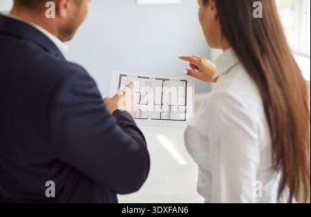 Male engineer, architect or realtor discussing apartment construction plan with young woman client. Stock Photo