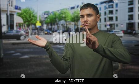 Man presenting open hand and pointing finger at invisible object in a busy city street intersection with cars and buildings; assertive instruction. Stock Photo