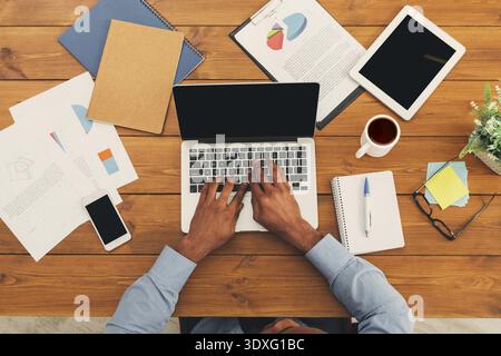 Working on a Laptop in a Workspace With Documents and Tools Around the Table Stock Photo