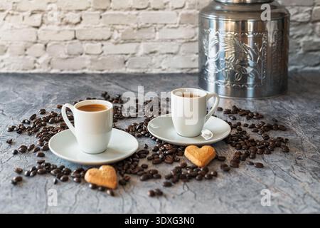 Two white espresso cups filled with freshly brewed coffee stand on saucers surrounded by roasted coffee beans. Stock Photo