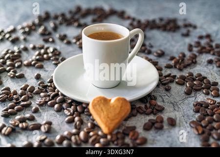 A white espresso cup filled with freshly brewed coffee stands on a saucer surrounded by roasted coffee beans. Stock Photo