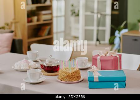 Birthday Cake with Candles and Wrapped Gifts Arranged on Dining Table Stock Photo