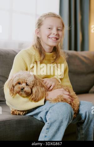 Vertical Portrait of Girl Smiling While Holding Small Dog on Sofa Indoors Stock Photo