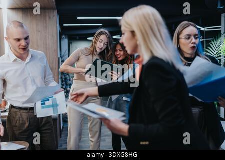 Group of diverse colleagues collaborating in an office, sharing documents and discussing charts Stock Photo
