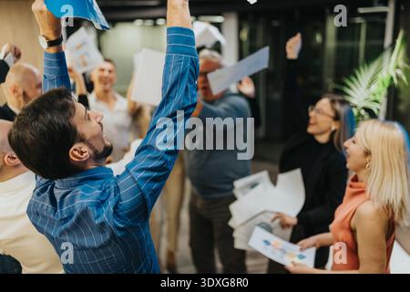 Office celebration: diverse team cheers, raises arms, and throws papers in triumph Stock Photo