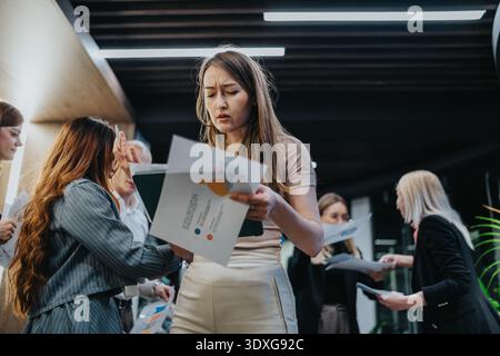 Young professional woman reviews documents at a busy networking event with colleagues. Stock Photo