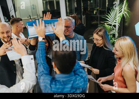 Group of colleagues celebrating in the office, raising a folder and sharing smiles Stock Photo