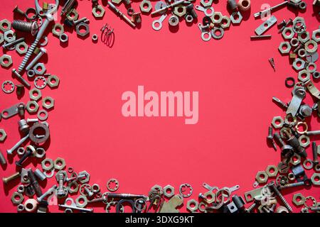 Assorted screws nuts and bolts forming frame on red background with copy space in center Stock Photo