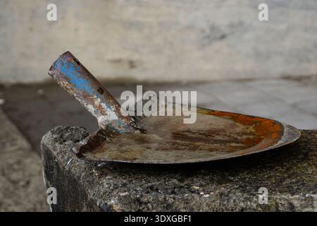 Rusty masonry trowel resting on a concrete surface, showing worn metal, corrosion and signs of construction work. Stock Photo