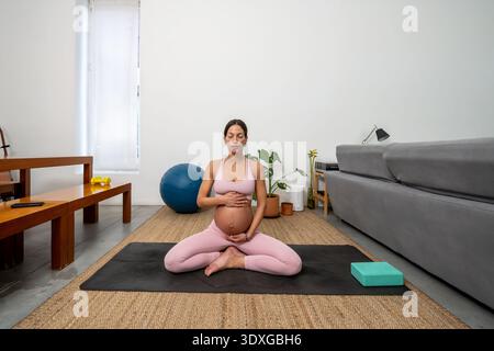 Pregnant Woman Meditating In Lotus Pose At Home Stock Photo