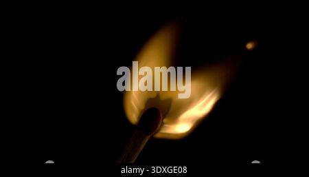 Flame from a lit match in darkness with smoke curling above and bright light shining below Stock Photo