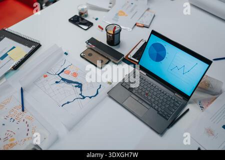 Business analysts use a laptop on a clean desk with charts, plans, and documents. Stock Photo