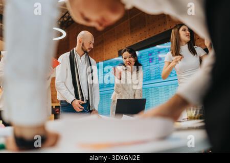 Collaborative office team discusses data and strategy around laptop in a modern workspace Stock Photo