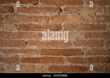 Rustic brick wall displaying a textured pattern of weathered red clay bricks with rough mortar, creating a solid and timeless architectural background Stock Photo