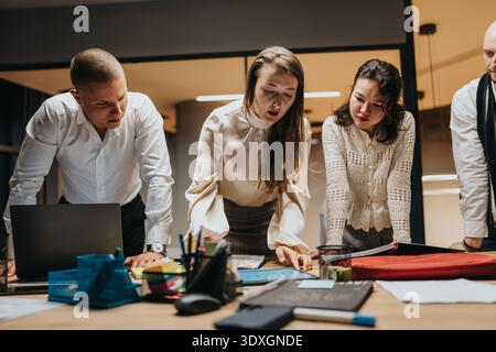 Business team collaborates around a table with laptop, papers, and notes in a modern office setting Stock Photo