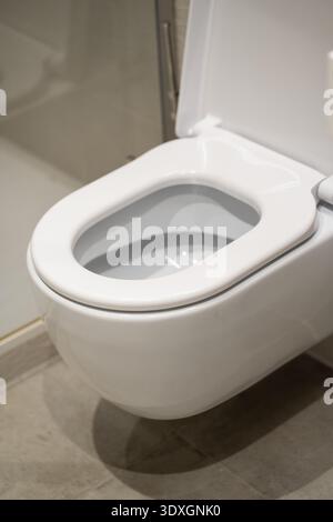 White wall-mounted modern toilet with lid open in a minimalist bathroom, focusing on hygiene, plumbing fixtures, and clean architectural design Stock Photo