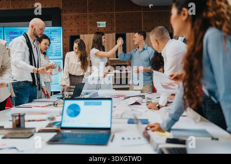 Team of business professionals collaborating in a busy office with charts and laptops Stock Photo