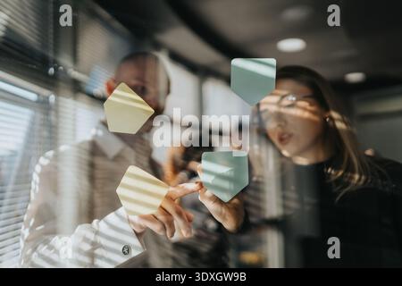 Two colleagues discuss sticky notes on a glass board in a modern office setting Stock Photo