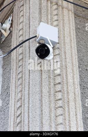 Low angle view of a modern security camera installed on a textured, fluted concrete wall. Neutral grey and white colors. Concept for surveillance, saf Stock Photo