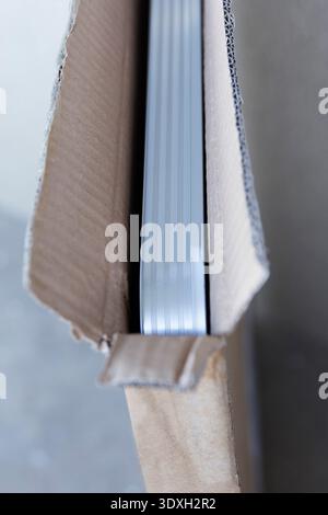 Abstract close-up of a new item, possibly framed art, inside an open cardboard box. Shallow depth of field highlights textures. Neutral colors, concep Stock Photo