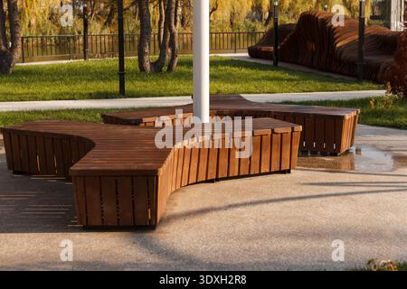 Modern wooden benches with unique architectural designs in a quiet park. Warm autumn sunlight creates long shadows on the pavement. A calm, empty urba Stock Photo