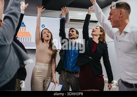 Team celebration in modern office during presentation with raised hands and smiles Stock Photo