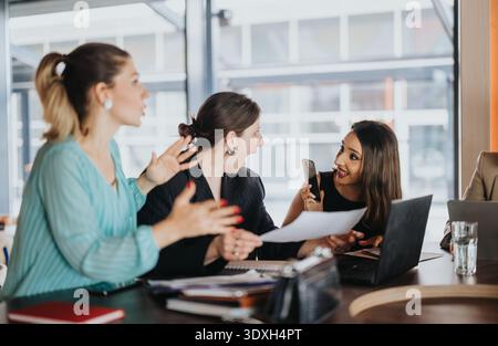 Businesswomen collaborating enthusiastically during a team meeting in a modern office setting Stock Photo
