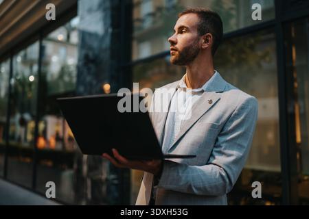 Professional businessman in a light gray suit with laptop outdoors in an urban setting Stock Photo