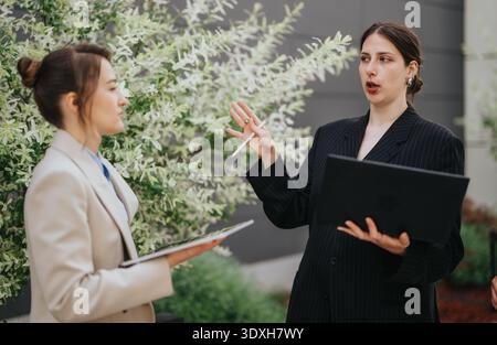 Two businesswomen collaborating outdoors with laptop and tablet during a professional discussion Stock Photo