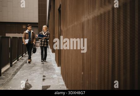 Two professionals walking together along an urban walkway outside a modern building with folders and notebooks Stock Photo