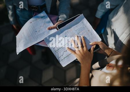 Business team reviews charts outdoors on a sunny day, discussing data and strategies. Stock Photo