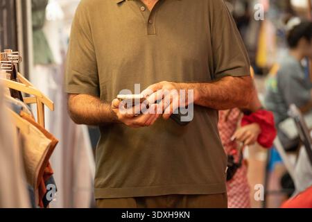 Man using smartphone in market while shopping, silhouette in strong sunlight, contrast light and shadow, close up, at Chatuchak Market. Stock Photo