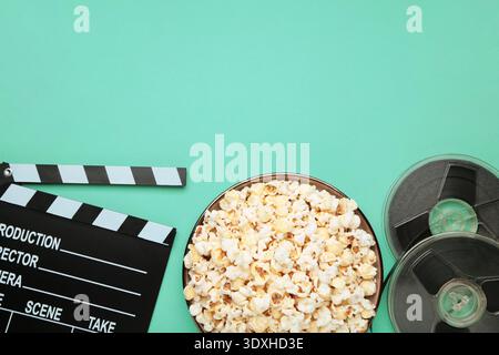 Movie clapper with popcorn and film reels on mint background. Top view Stock Photo
