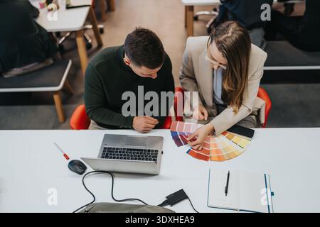 Two designers collaborate over color swatches and a laptop at a bright modern desk Stock Photo
