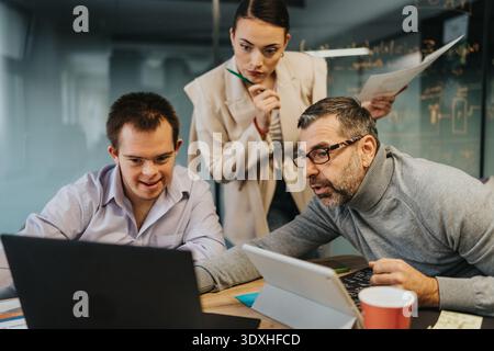Team of colleagues collaborates at a desk reviewing laptop and tablet in office Stock Photo
