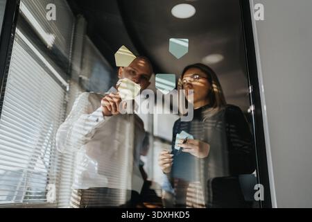Business professionals collaborate in a glass-walled office using sticky notes for idea brainstorming Stock Photo