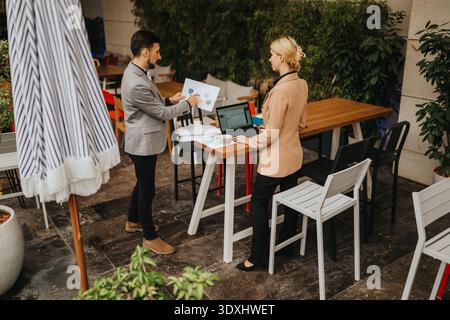 Business partners discuss presentation outdoors at a cafe with laptop and charts Stock Photo