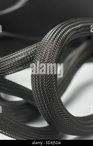 coiled black nylon mesh cable sleeve in close-up macro, flexible woven texture cord with detailed braided pattern in soft focus, electronics cable Stock Photo