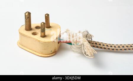 old three pin plug and frayed power cord isolated white background, exposed internal wires and tan black braided sleeve with torn white fibers Stock Photo
