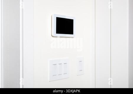 Smart home tablet on wall with light switches. Smart home technology device in modern home. Digital remote control system for air conditioning, securi Stock Photo