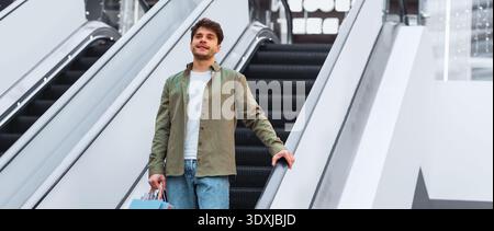 Young Man Riding Escalator While Holding Shopping Bags in a Mall During Daytime Stock Photo