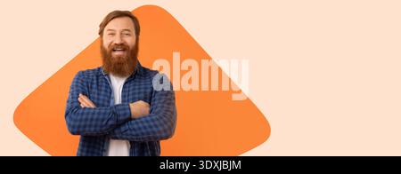 Bearded Man Smiles While Standing Against Orange Background With Crossed Arms Stock Photo