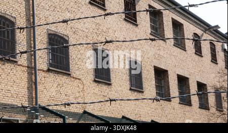 Old prison building with bars on the windows and barbed wire fence in the foreground. Stock Photo