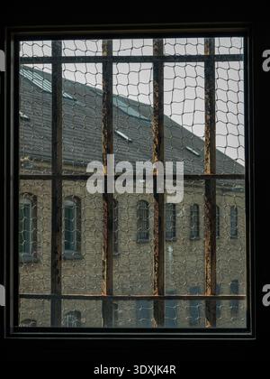 View through cell window in a jail with rusty iron bars to the old prison buildings outside. Stock Photo