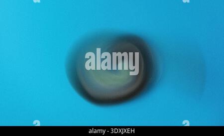A blurry close up of a dark circular object centered on a light blue background with soft lighting Stock Photo
