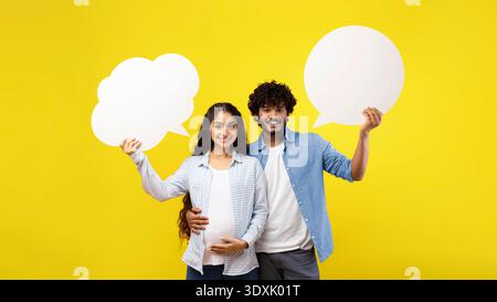Couple Holds Speech Bubbles in Front of a Bright Yellow Background During Pregnancy Celebration Stock Photo